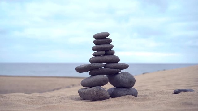 The cairn stands on the sand. The hand adds the last stone to finish the cairn. Slow motion