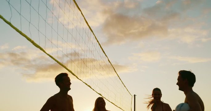 Friends cheer and put hands up at volleyball net, slow motion cinematic sunset sport