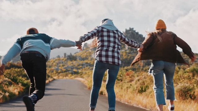 young multi ethnic friends longboarding together holding hands riding skateboard cruising downhill on countryside road having fun enjoying relaxed summer vacation