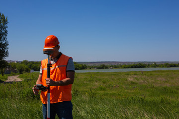 Professional Male Land Surveyor Measures Ground Control Point Using a GPS Rover. Green Field on a...
