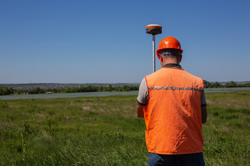 Professional Male Land Surveyor Measures Ground Control Point Using a GPS Rover. Green Field on a...