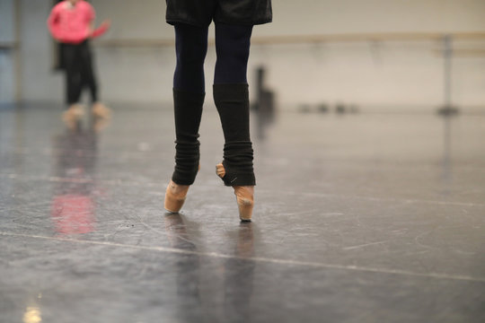 Legs of a ballerina standing on pointe in warm socks at a rehearsal in the hall
