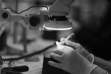 The hands of a dental technician processing a prosthesis with a drill under the microscope