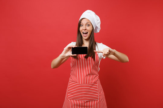 Housewife female chef cook or baker in striped apron white t-shirt toque chefs hat isolated on red wall background. Woman hold cellphone blank screen for promotional content Mock up copy space concept