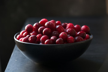 Frozen cranberries in dark bowl on black.