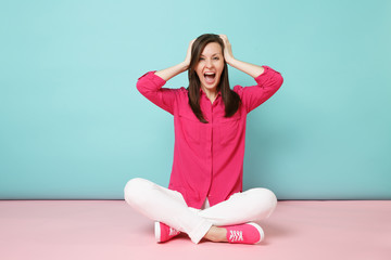 Fototapeta na wymiar Full length portrait of smiling young woman in rose shirt blouse, white pants sitting on floor isolated on bright pink blue pastel wall background studio. Fashion lifestyle concept. Mock up copy space