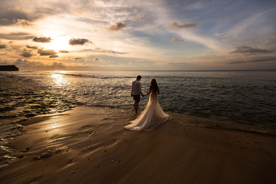 Bride and groom go to sea on the beach at sunset