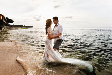 Bride and groom embracing look at each other standing in the sea water on the beach