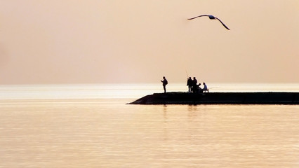 .Calm sea on sunset. People at the pier silhouette. People unrecognizable. Soft focus