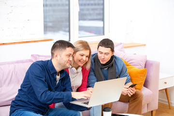 Friends sit on the couch, chatting and using a smartphone, desktop computer, laptop.