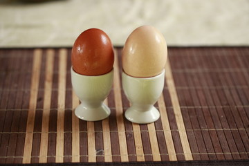 different colors eggs and white glass egg holders, on a brown mat: rustic breakfast