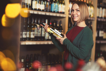 Picture of girl with bottle in her hands on blurred background of shelves with bottles of wine