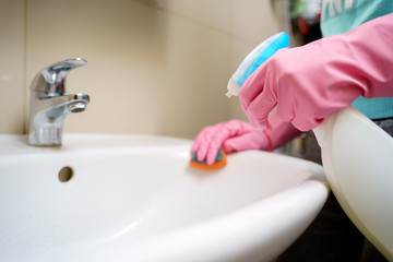 Image of hands in pink rubber gloves washing sink in bath