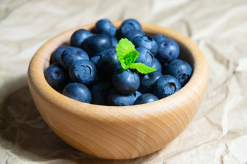 A wooden bowl full of blueberries with plain soft background decorated by fresh mint