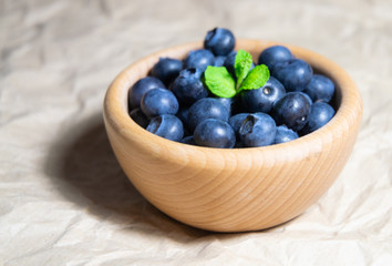 A wooden bowl full of blueberries with plain soft background decorated by fresh mint