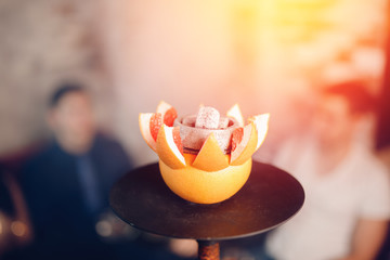 Change coals and tobacco hookah on fruit. In background group of friends people are resting and smoking shisha