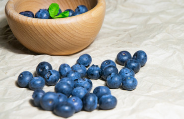An isolated wooden bowl full of blueberries with plain soft background decorated by fresh mint and with a few blueberries around