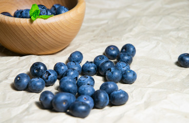 An isolated wooden bowl full of blueberries with plain soft background decorated by fresh mint and with a few blueberries around