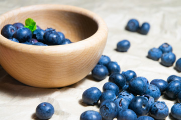 An isolated wooden bowl full of blueberries with plain soft background decorated by fresh mint and with a few blueberries around