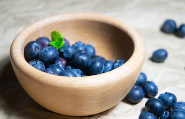 An isolated wooden bowl full of blueberries with plain soft background decorated by fresh mint and with a few blueberries around