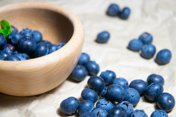 An isolated wooden bowl full of blueberries with plain soft background decorated by fresh mint and with a few blueberries around