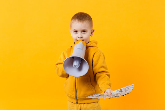 Little happy kid boy in yellow clothes hold fan of money in dollar banknotes, megaphone isolated on orange wall background, children studio portrait. Childhood lifestyle concept. Mock up copy space.