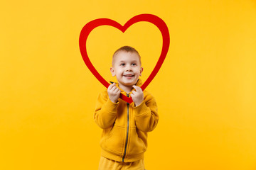 Little kid boy 3-4 years old wearing yellow clothes hold red heart isolated on orange wall background, children studio portrait. People sincere emotions childhood lifestyle concept. Mock up copy space