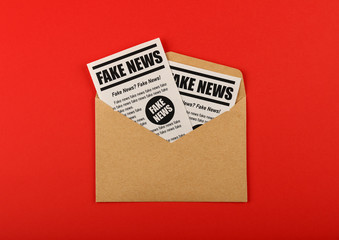 Envelope with FAKE NEWS newspapers over red