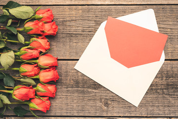 Red, fragrant roses arranged in a row against the background of old, natural boards. Stylish composition of flowers with free space and open envelope for text. Frame made of wood and plants.