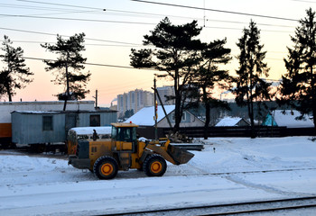 Front-end loader with wheels on a construction site in winter against the backdrop of sunset and spruce trees. Diesel bulldozer with bucket