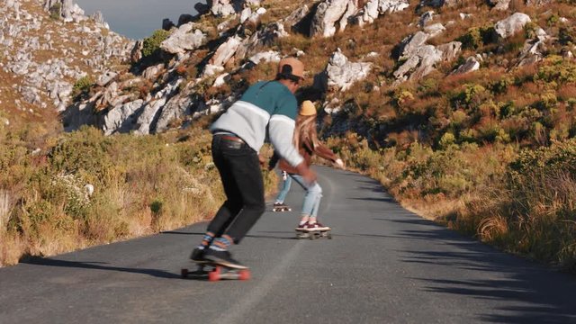 young multi ethnic friends longboarding together riding skateboard cruising downhill on countryside road having fun enjoying relaxed summer vacation