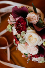  bridal bouquet with ribbons of roses, peonies and claret callas on the table. with wedding rings.