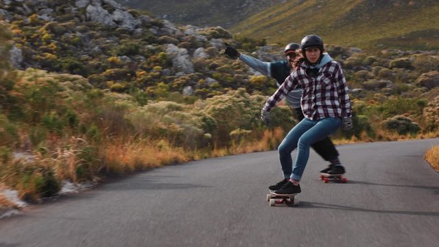 happy multi ethnic friends longboarding together cruising fast racing having fun riding on countryside road skateboarding wearing protective helmet summer vacation sport