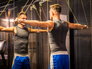 Muscular young man, training shoulders on gym cable machine