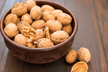 walnuts lie in a bowl, next to them are chopped nuts on a wooden floor