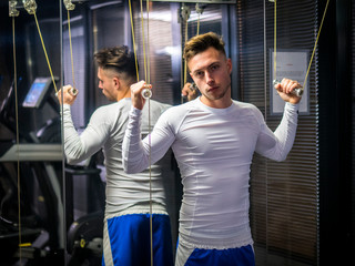 Obraz premium Muscular young man, training shoulders on gym cable machine