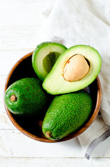 Avocado in a wooden bowl on a white wooden background