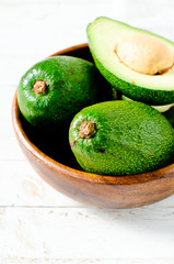 Avocado in a wooden bowl on a white wooden background