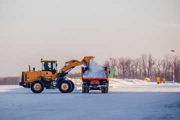 Snow cleaning in airport. Excavator loads snow into dump truck