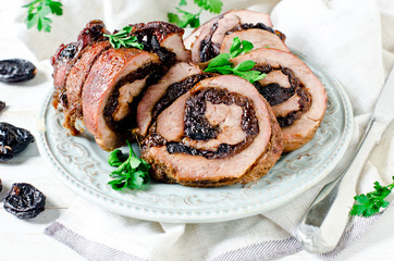 Baked turkey roll with prunes on a plate on a white wooden table