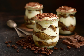 Traditional italian dessert tiramisu with chocolate sauce in a vintage glass jars on a dark rustic slate, stone or concrete background.