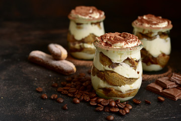 Traditional italian dessert tiramisu with chocolate sauce in a vintage glass jars on a dark rustic slate, stone or concrete background.