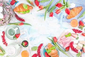 Sweet spring breakfast with croissants and bacon on a light background. A bouquet of red tulips and fresh berries of strawberries and currants. The concept of holiday celebration.