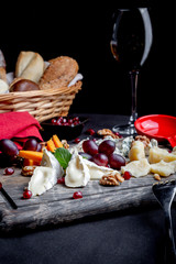 Cheese plate served with grapes, honey, nuts and glass of wine with bread basket on a wooden background. Various types of cheese.