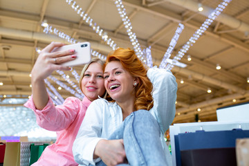 Obraz premium Two happy friends is taking selfie while shopping in mall.
