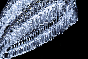 A large number of glasses in the shape of an oval hang on the holder at the bar counter on a dark...