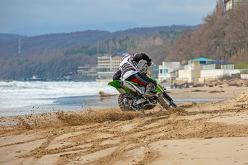 Obraz premium Motorcyclist in a protective suit rides a motorcycle on the sea, splashes fly from under the wheels.