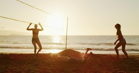 Group of friends playing beach volleyball at sunset, athletic man dives to save volleyball, slowmotion