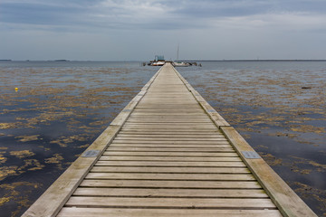 Long, wooden dock in the ocean. Dock leading to the boats. Cloudy day.