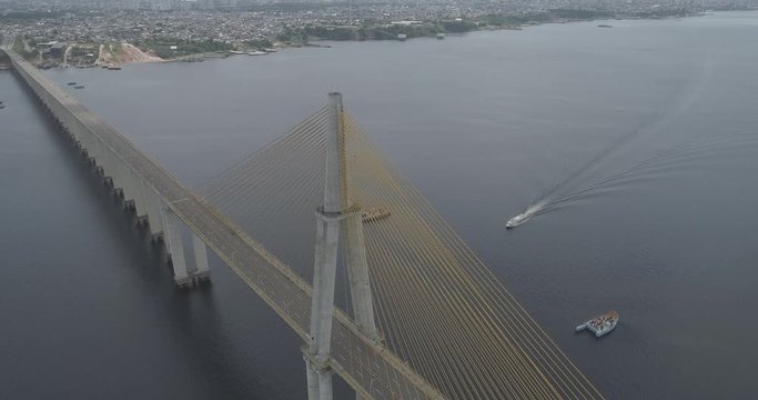 High aerial circling the cable-stayed Rio Negro Bridge that links the cities of Manaus and Iranduba in the Brazilian Amazon as a boat approaches underneath